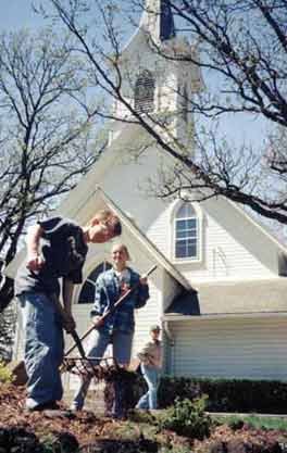 Photo of a boy and girl doing work on a flower bed
              in front of the church.